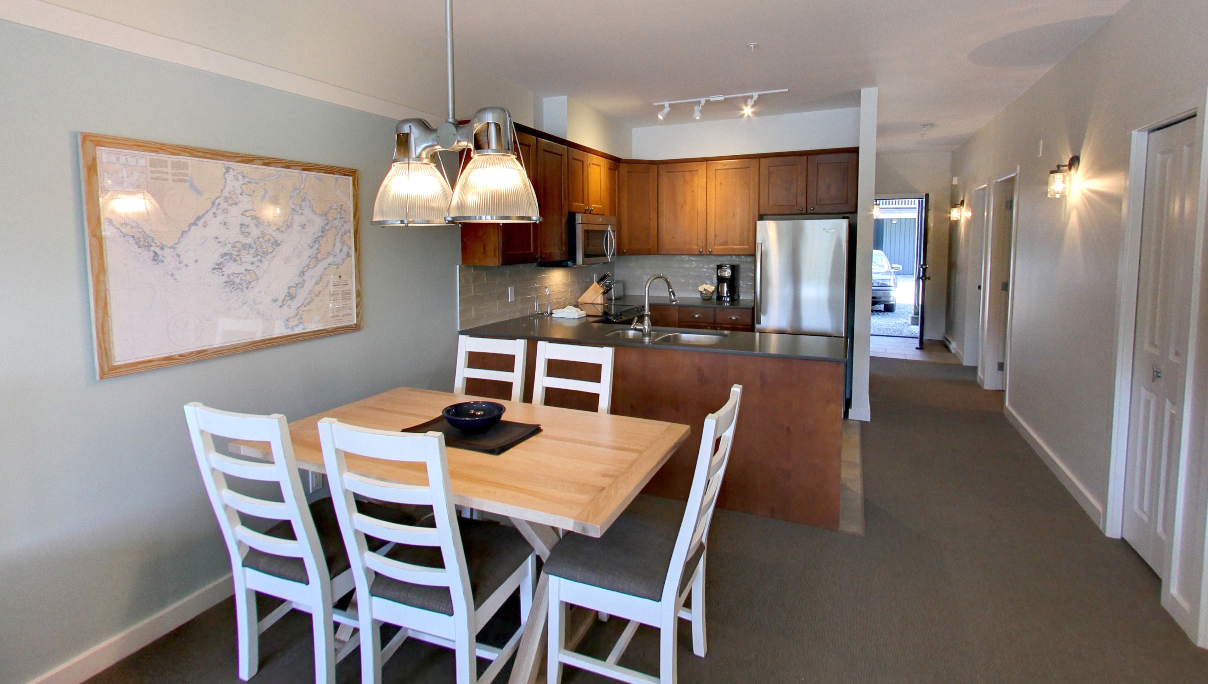 A modern kitchen with wooden cabinets, a stainless steel refrigerator, and a dining area with a wooden table and white chairs.