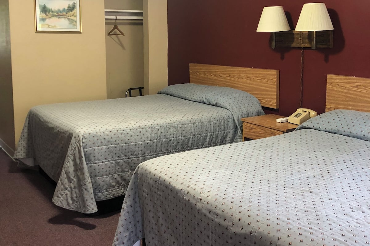 Une chambre d’hôtel avec deux lits, une tête de lit en bois, une table de chevet avec une lampe, un téléphone et un tableau encadré au mur.