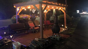 A covered outdoor seating area with chairs, a fire pit, and string lights. - Laurel Park Inn (Maggie Valley)