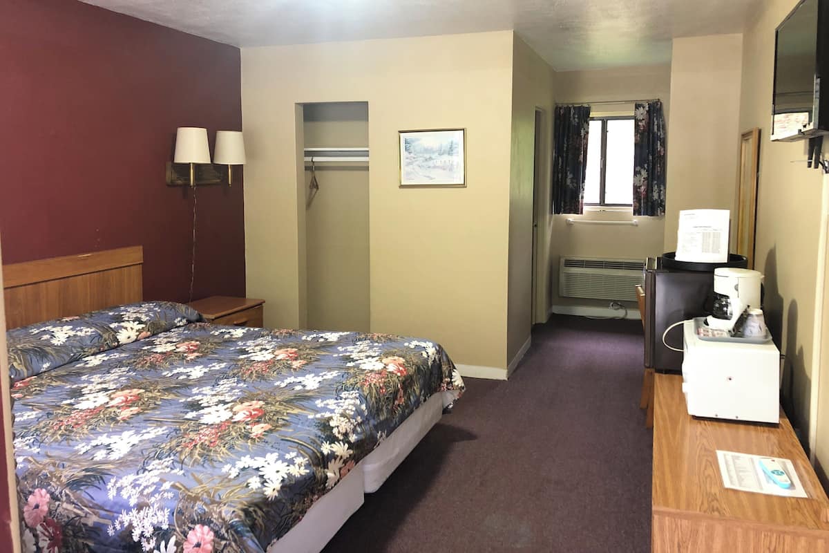 Une chambre d’hôtel comprenant un lit, un bureau, un miroir, une fenêtre avec des rideaux et un petit coin cuisine.