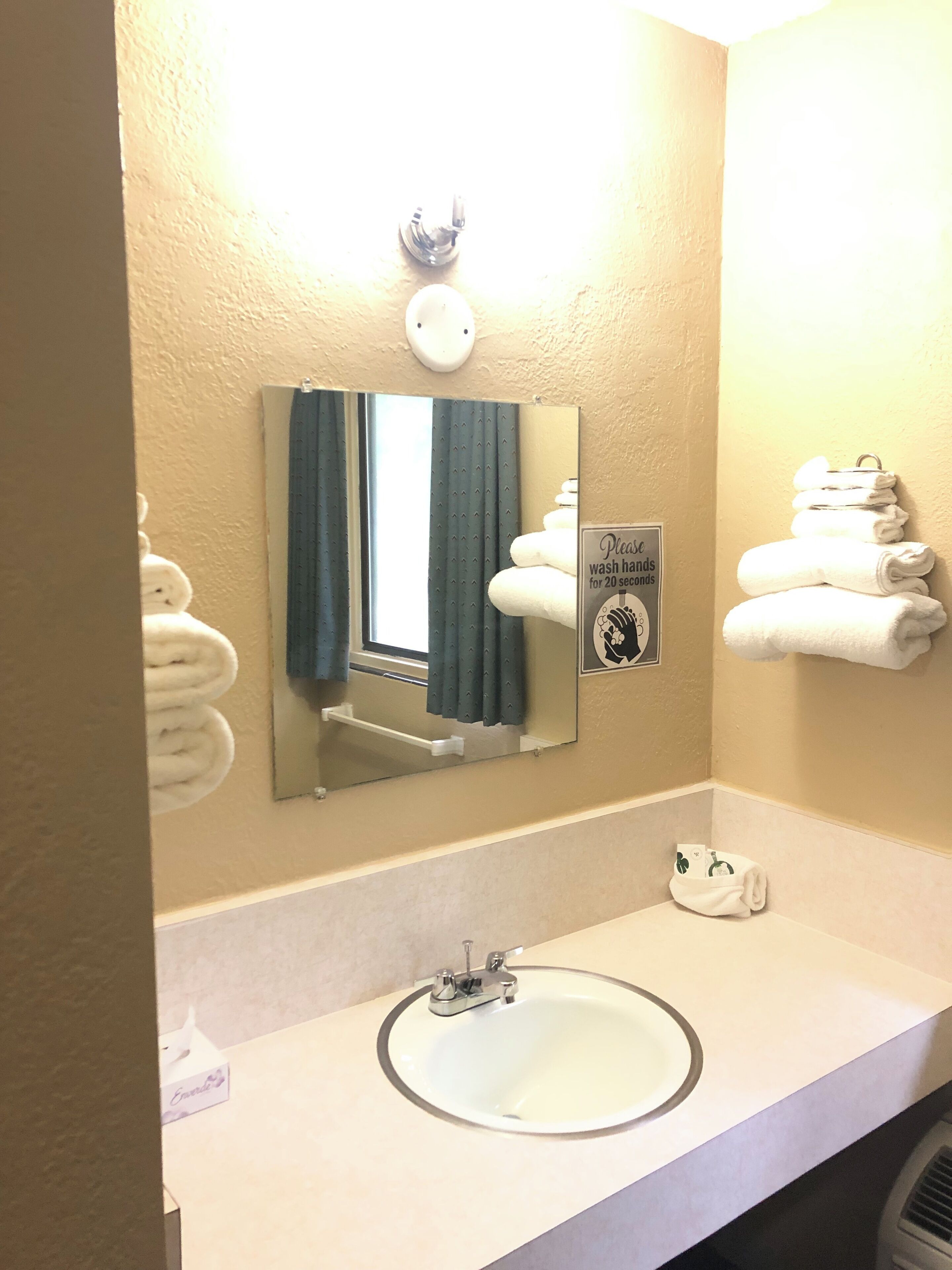 Un baño con lavabo, espejo, toallero y un cartel que indica lavarse las manos durante 20 segundos.