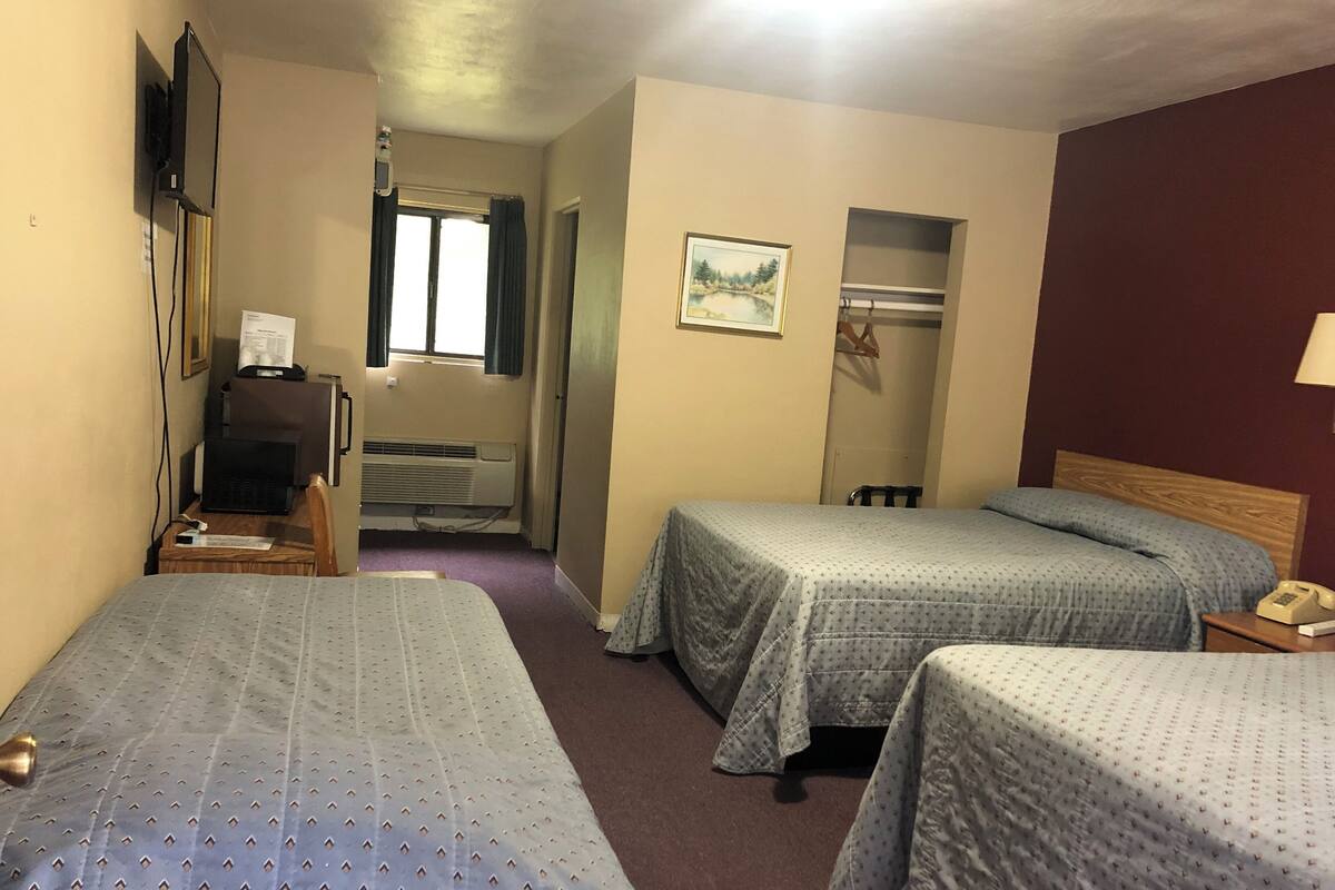 Une chambre d’hôtel avec deux lits, un bureau avec un ordinateur, une télévision et une fenêtre avec des rideaux.