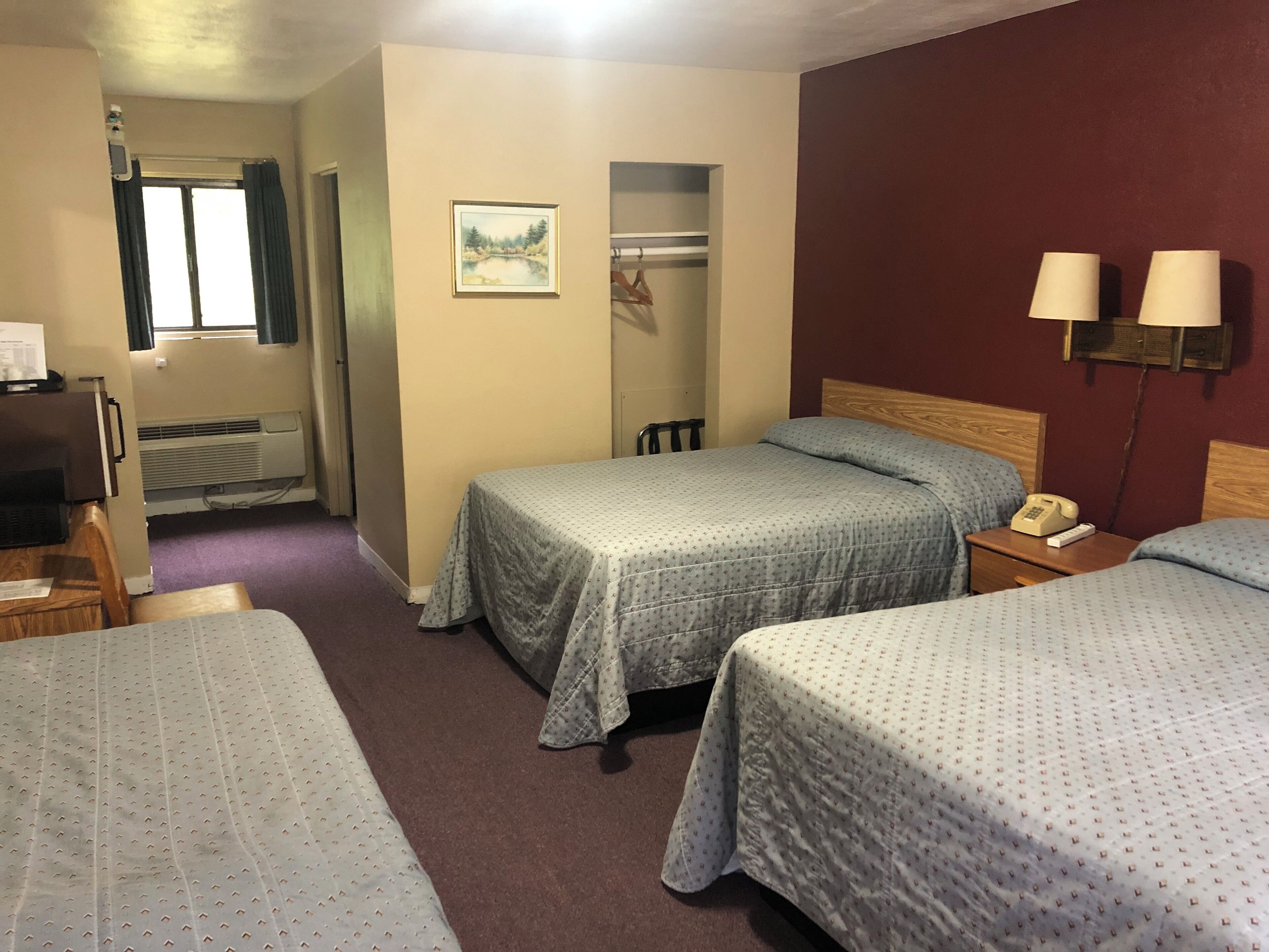 Quarto de hotel com duas camas, uma mesa, um telefone e um quadro na parede.