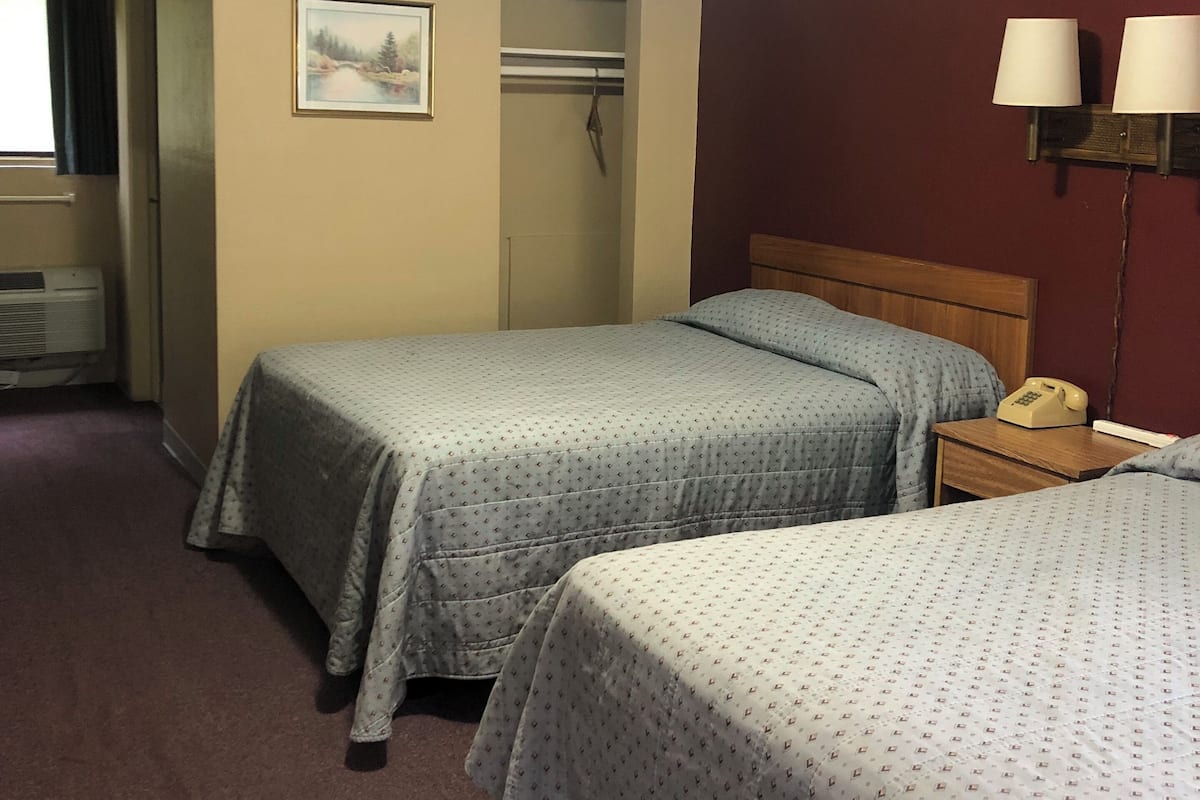 Une chambre d’hôtel avec deux lits, un placard, un tableau et un téléphone sur une table de chevet.