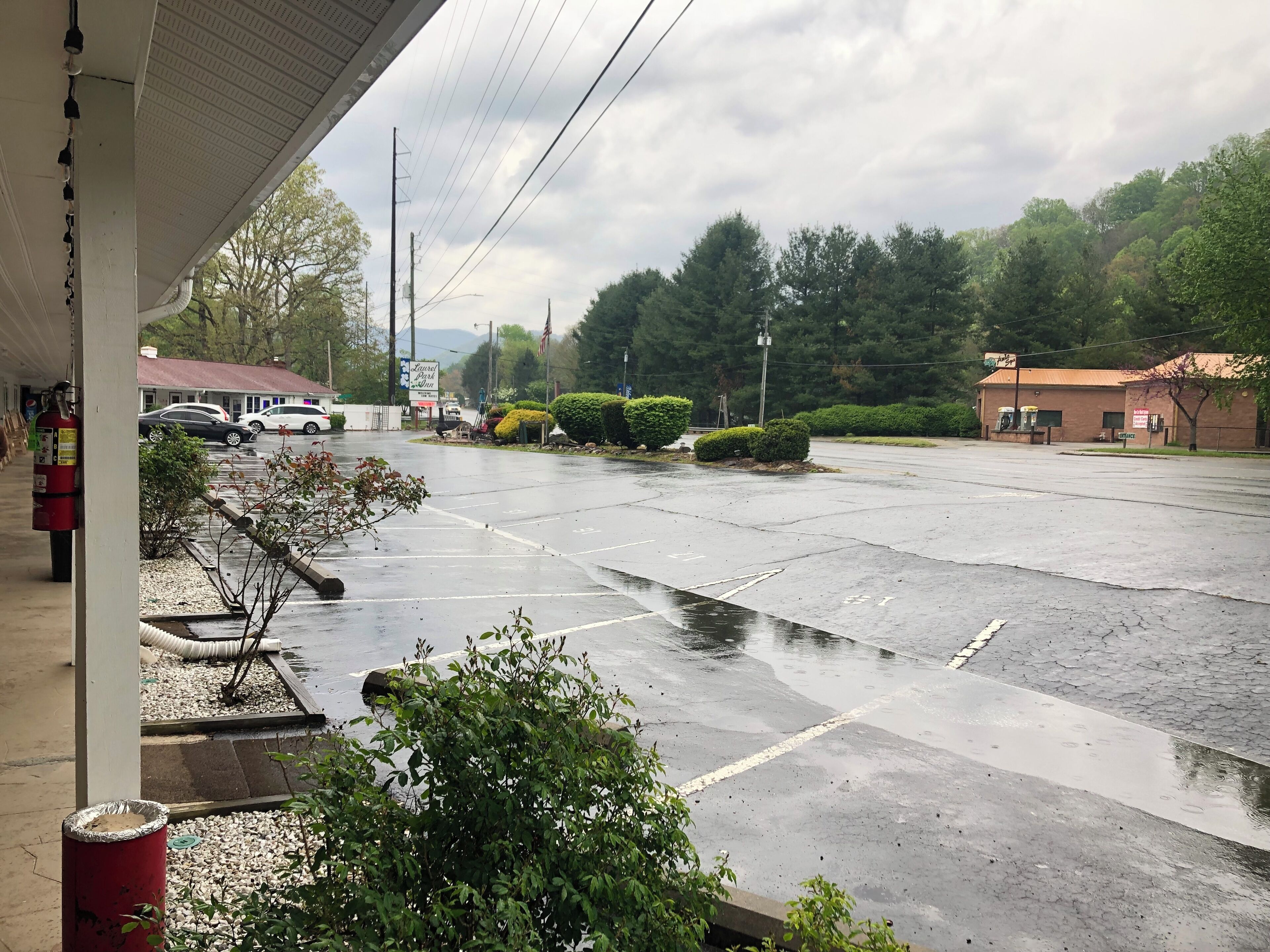 A parking lot with a building in the background, a fire extinguisher, and some greenery.