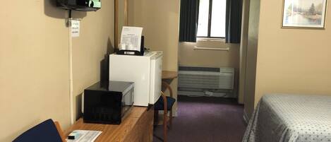 A hotel room with a wooden desk, a chair, a bed with a patterned bedspread, a television mounted on the wall, and a window with curtains.