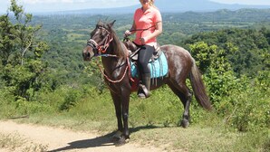 A person riding a horse on a dirt path with a scenic view of green hills and a mountain in the background. - Chez Nous B&B (San Juan del Sur)