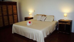 A neatly made bed with a white bedspread and pillows, two bedside tables with lamps, and a wooden wardrobe. - Chez Nous B&B (San Juan del Sur)