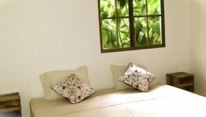 A bedroom with a bed, two pillows, a window, and a nightstand. - Chez Nous B&B (San Juan del Sur)