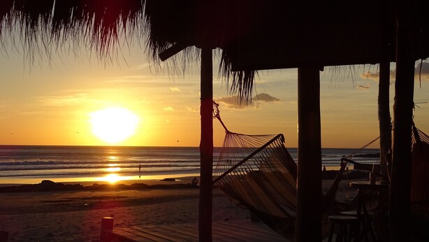 A beach scene with a hammock and a wooden deck. - Chez Nous B&B (San Juan del Sur)