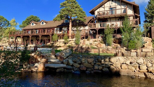 A two-story lodge with a stone foundation, wooden balconies, and a small waterfall feature. - The Landing at Estes Park - Riverside Retreat (Estes Park)
