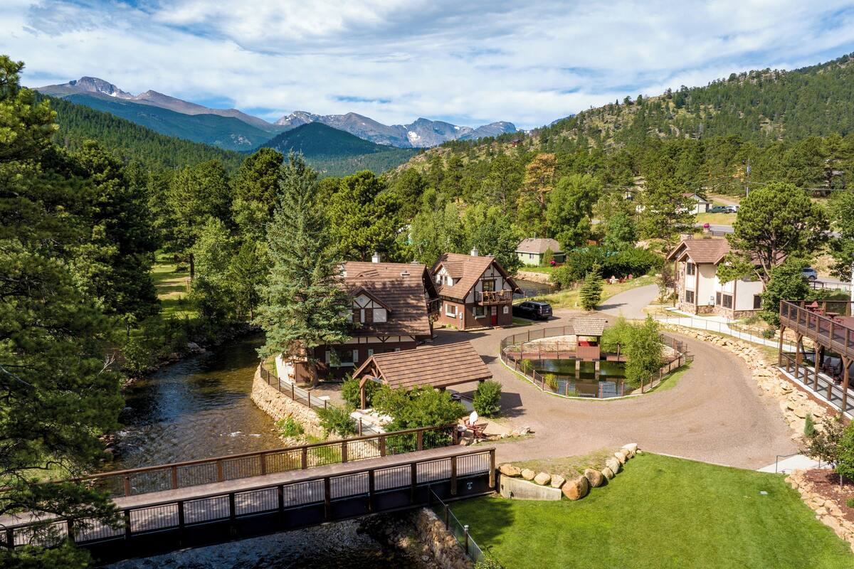 A lodge with a wooden deck, a small pond, and a view of mountains.