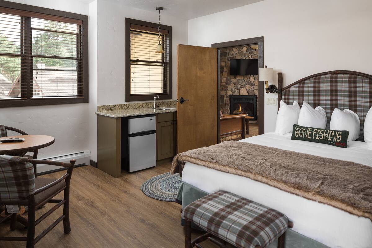 A bedroom with a bed, a small desk, a chair, a fireplace, and a window with blinds.