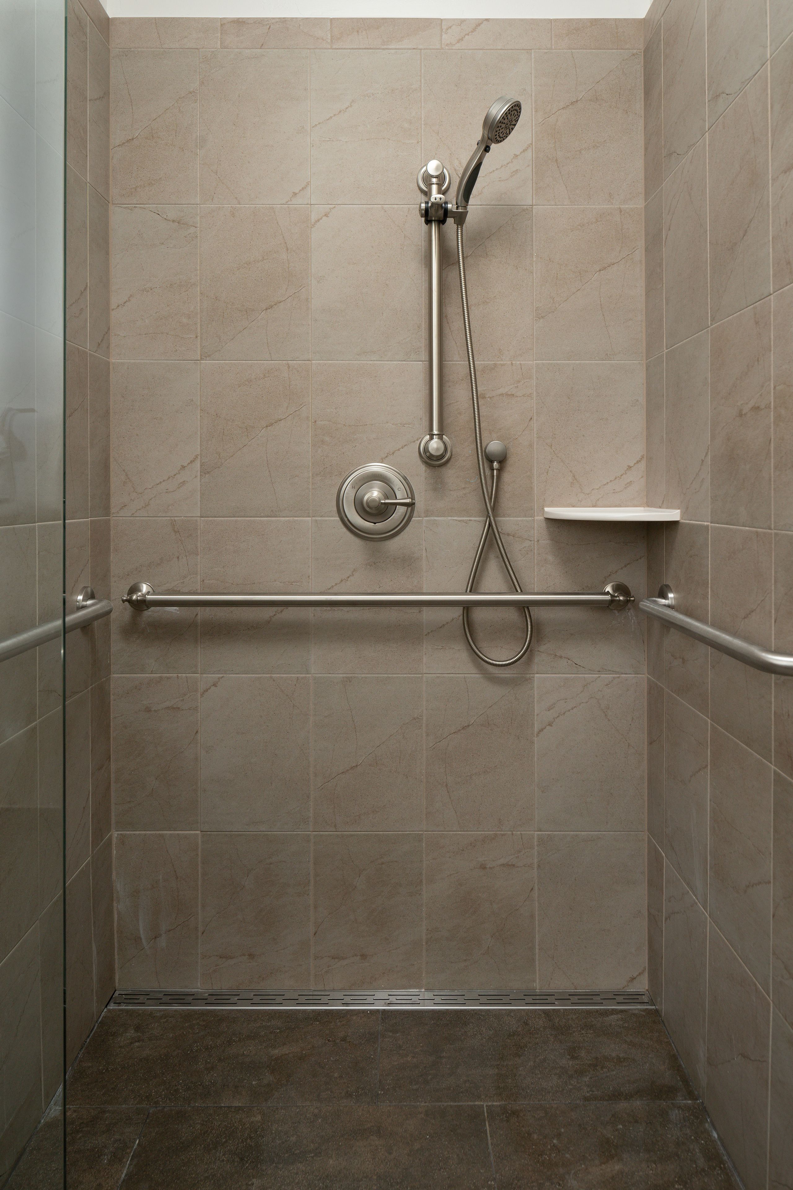 A shower with a handheld showerhead, a wall-mounted control, and a grab bar.