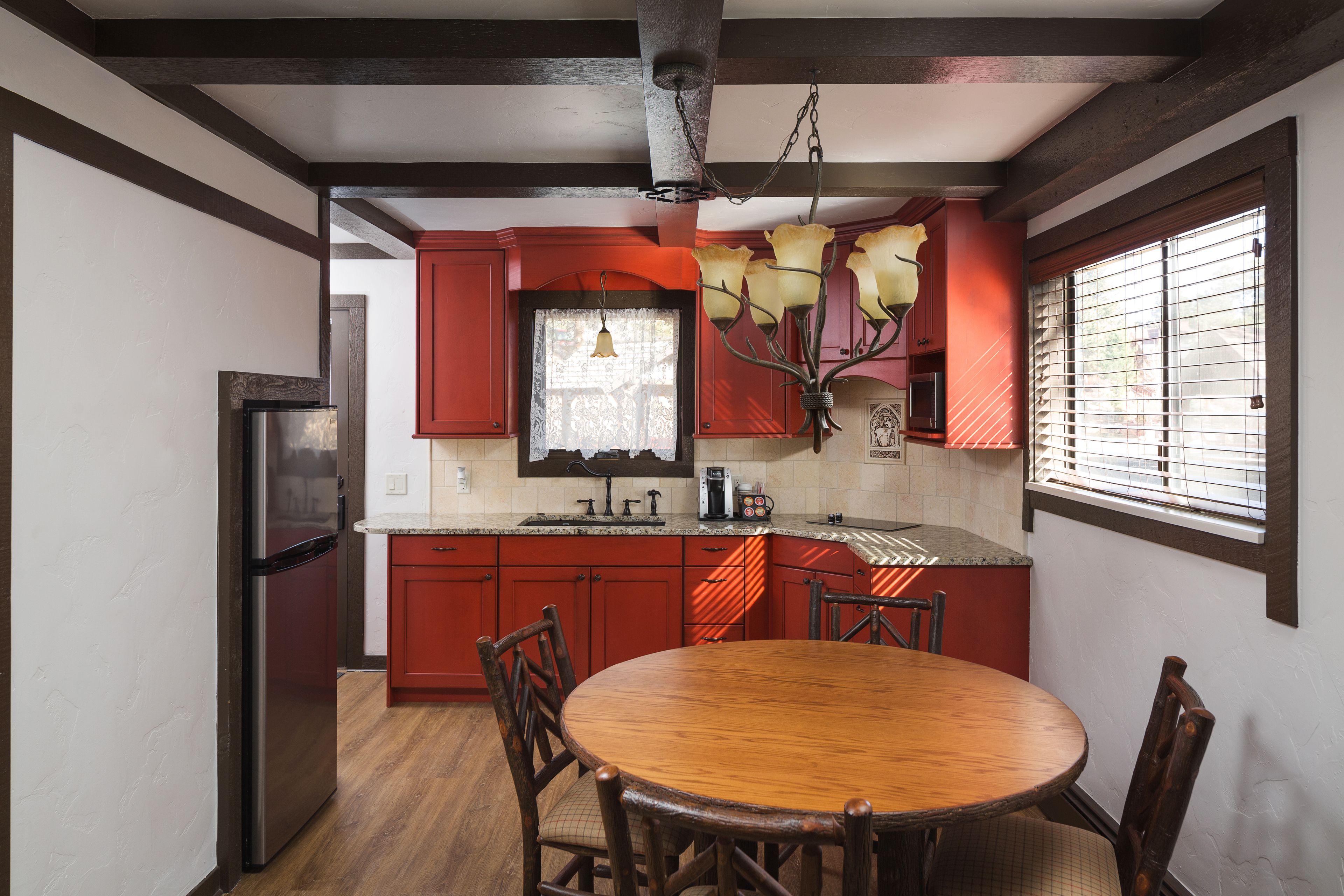 A kitchen with red cabinets, a stainless steel refrigerator, a wooden dining table with chairs, and a hanging light fixture.