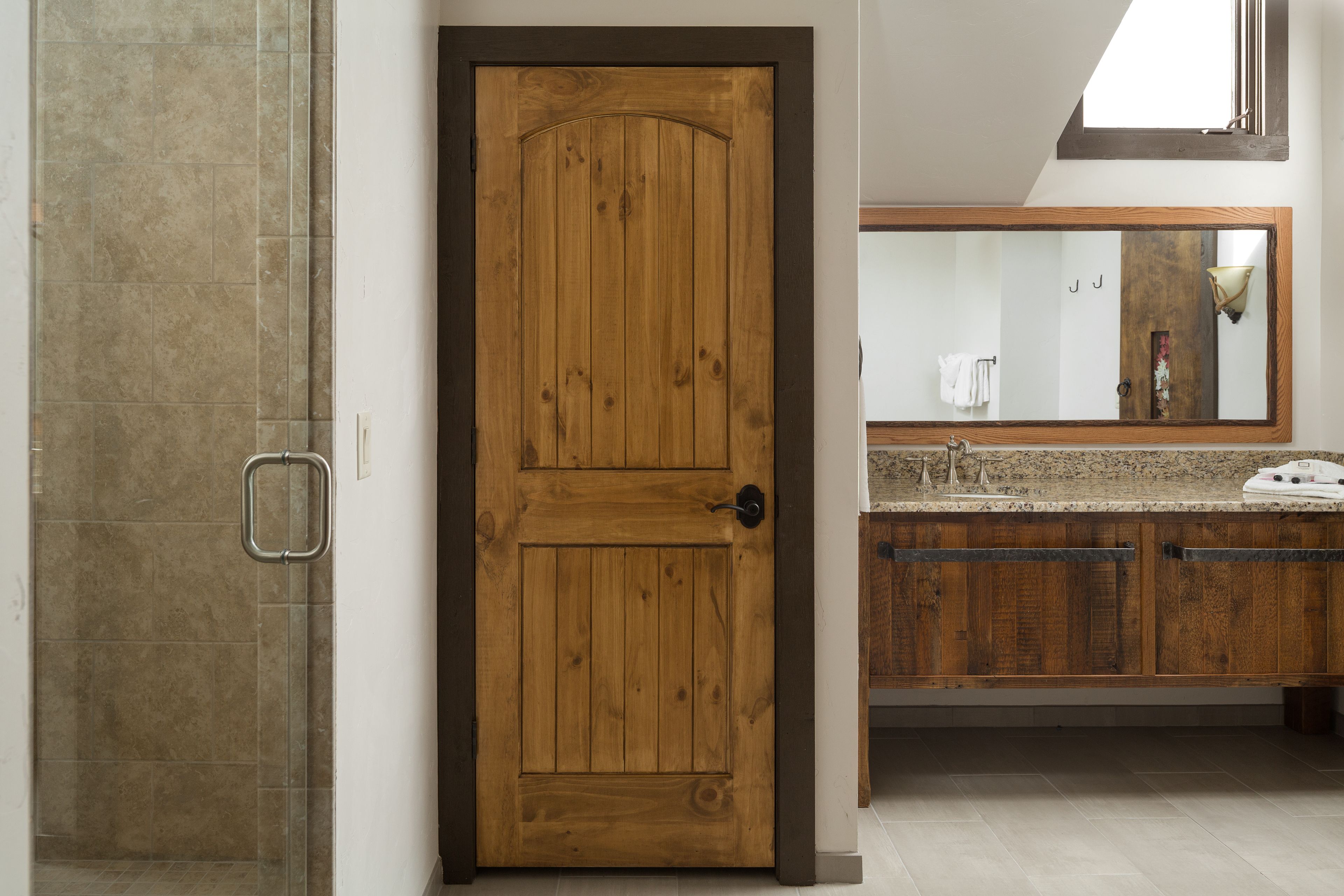 A bathroom with a wooden door, a shower area, and a vanity with a mirror.