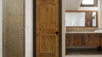 A bathroom with a wooden door, a shower area, and a vanity with a mirror.