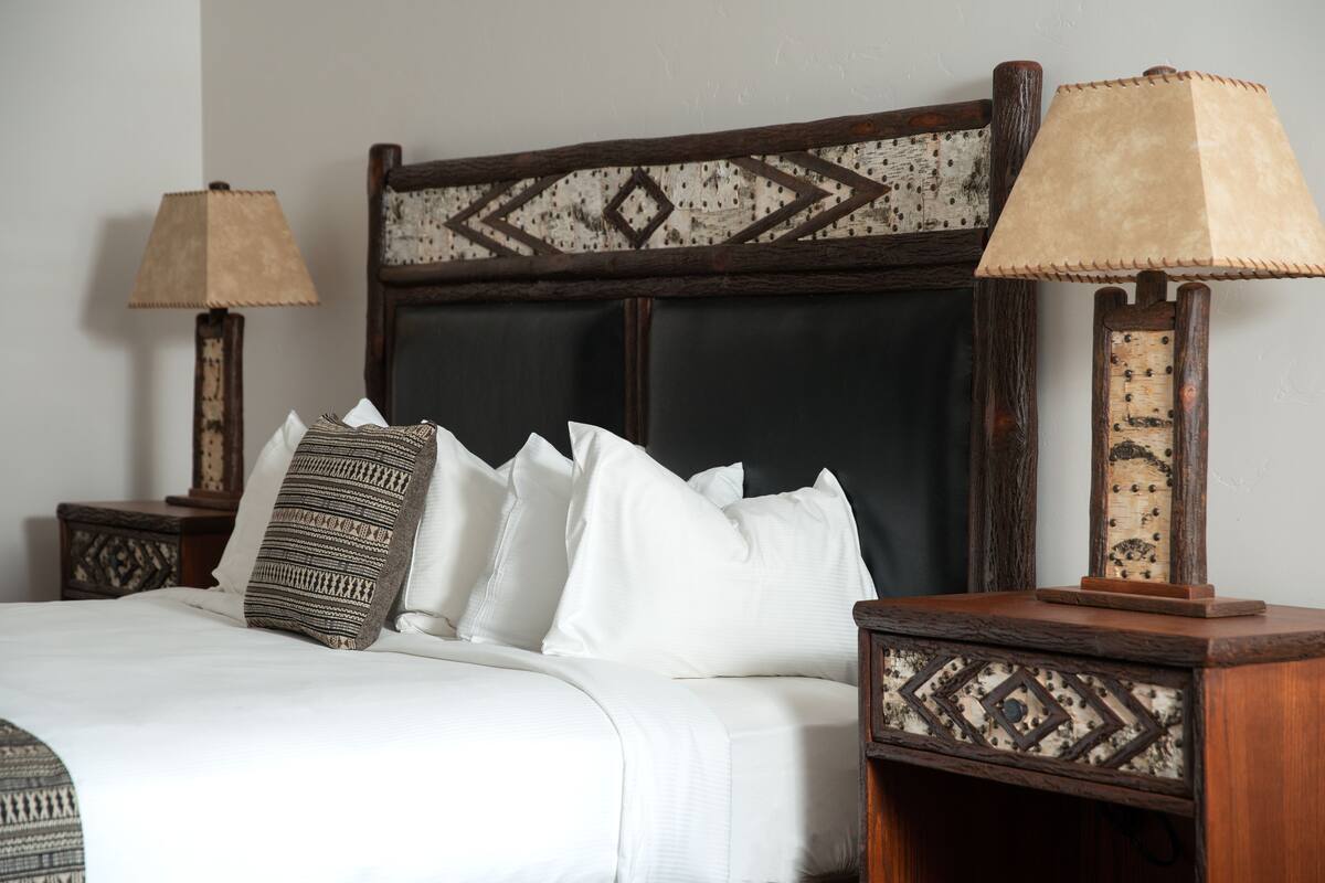 A bed with white linens and multiple pillows, flanked by two wooden nightstands with lamps.