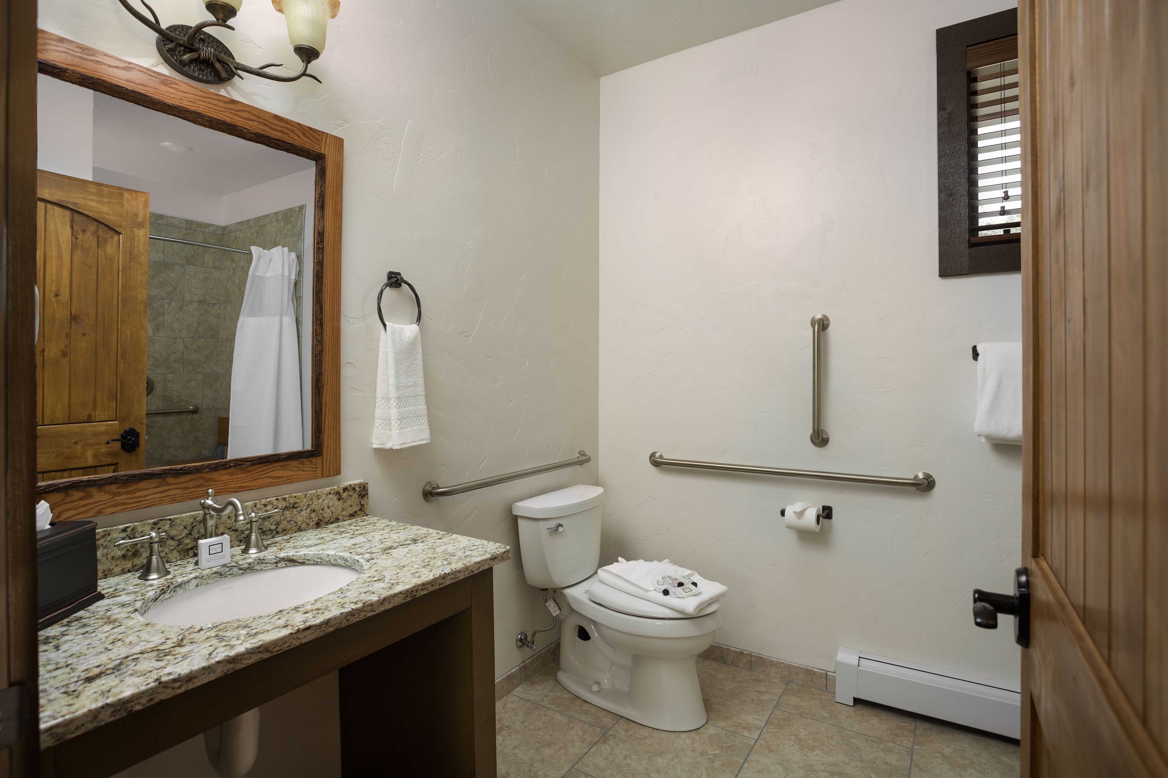 A bathroom with a sink, toilet, and mirror. There are handrails and a towel rack.
