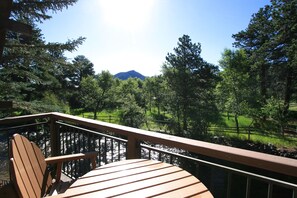 A wooden deck with a chair, overlooking a forested area and a mountain in the distance. - The Landing at Estes Park - Riverside Retreat (Estes Park)