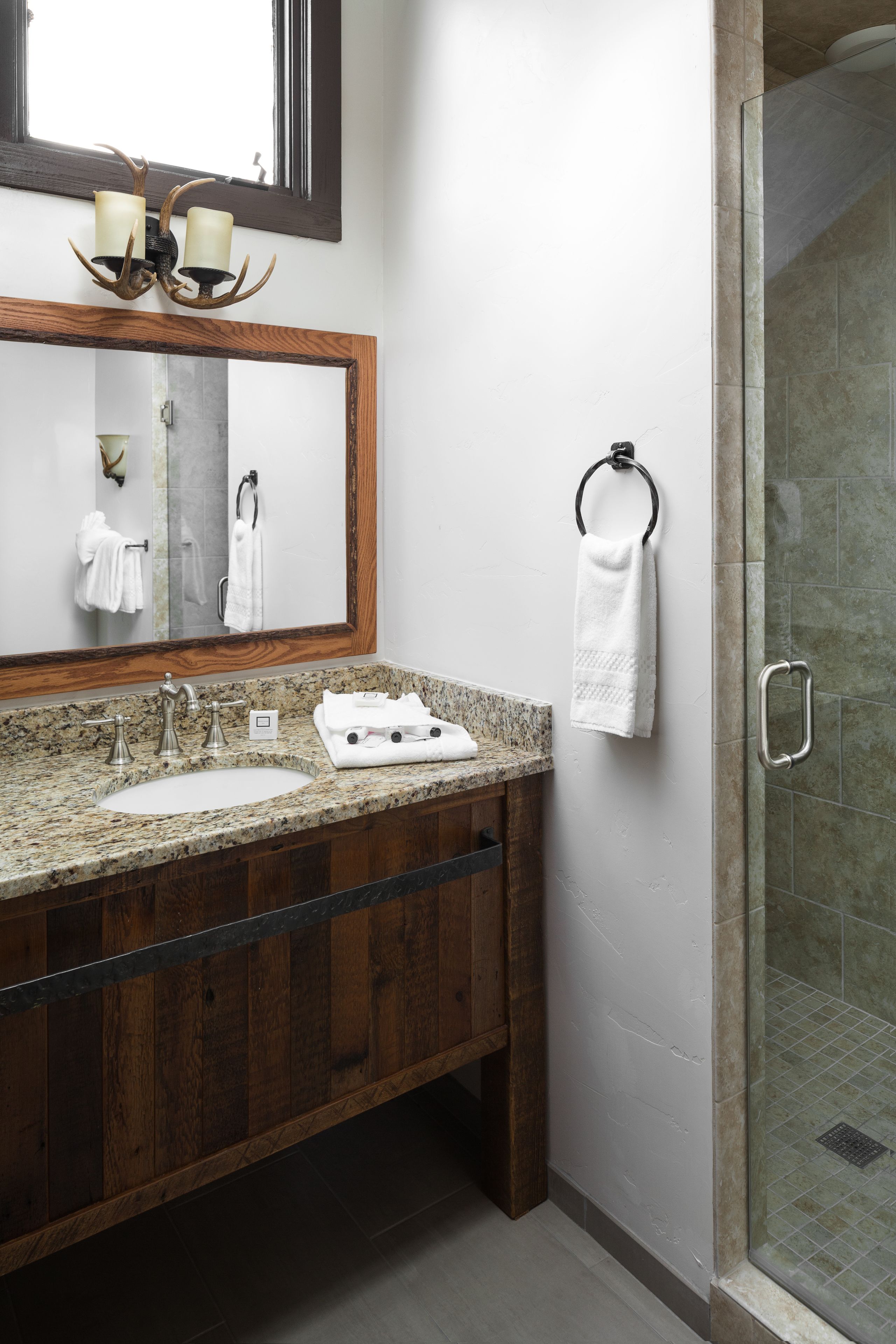 A bathroom with a granite countertop sink, wooden vanity, a large mirror, and a glass shower enclosure.