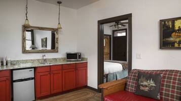 A compact kitchen with red cabinets, a microwave, and a refrigerator. There is a wooden dining table and a red couch with a decorative pillow.