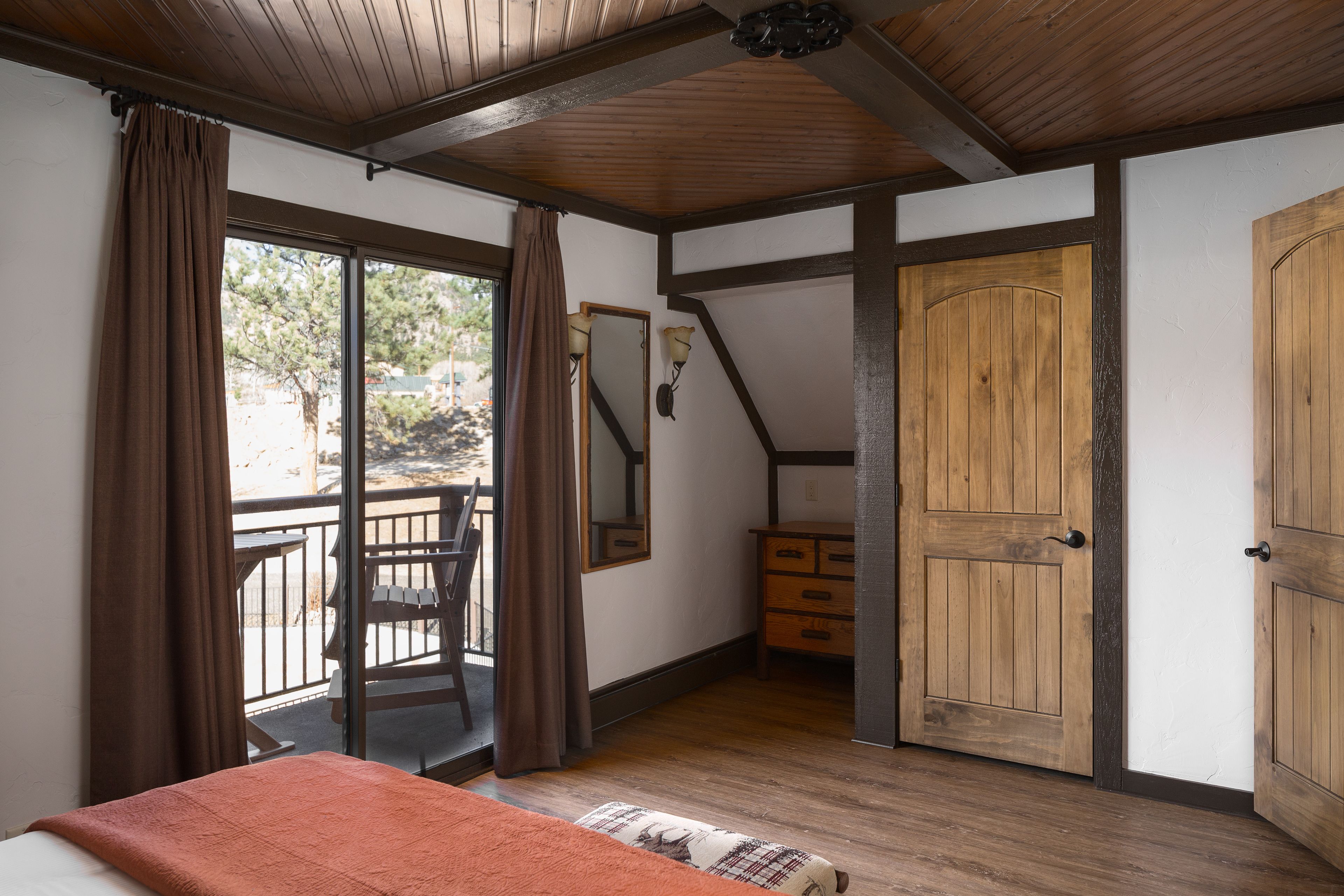 Une chambre avec un plafond en bois, un lit recouvert d’une couverture rouge, une commode et une porte coulissante.