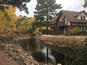 A riverside lodge with a stone retaining wall, a wooden deck, and a large tree. - The Landing at Estes Park - Riverside Retreat (Estes Park)