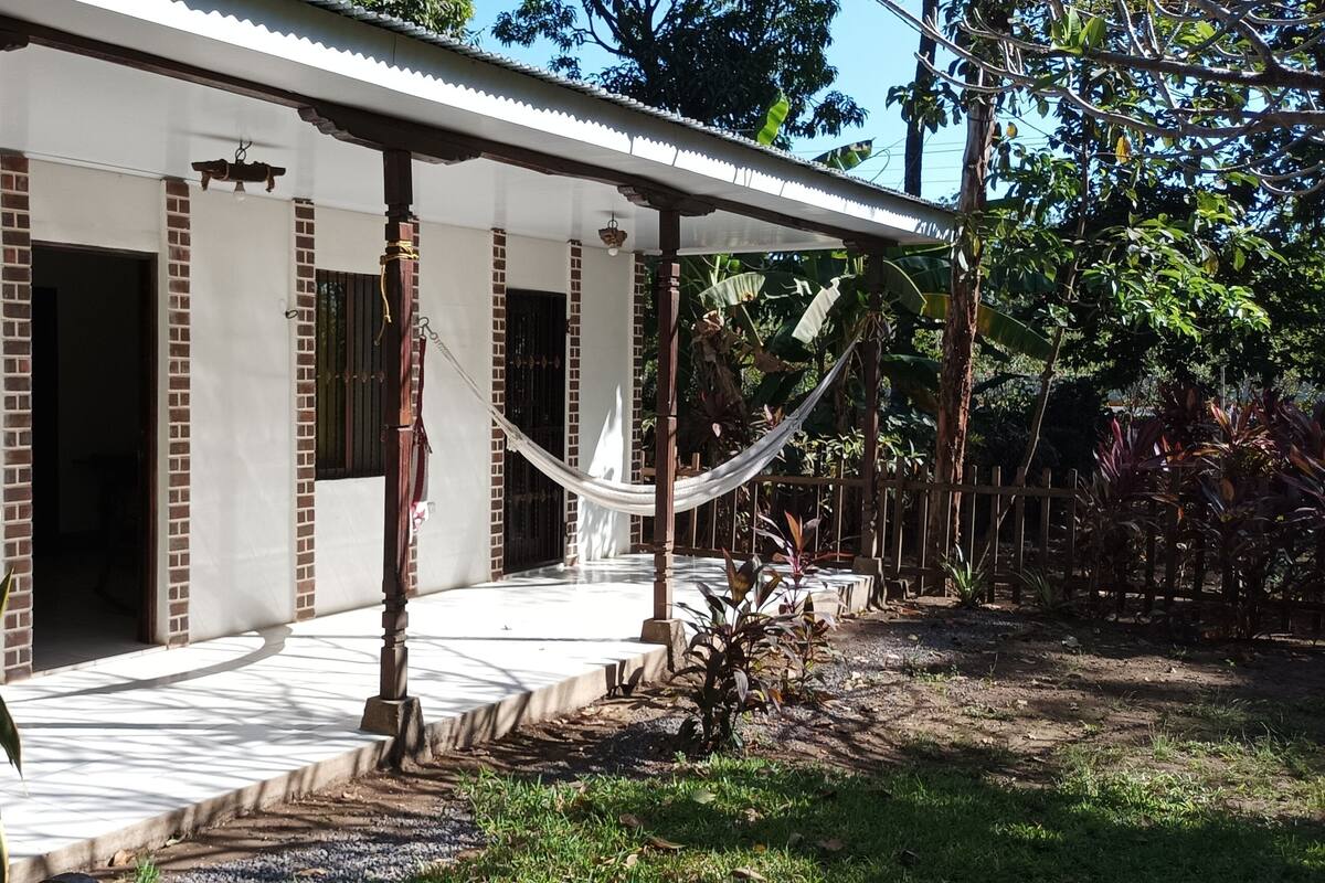 A house named "Casa Flor de Saguanjoche" with a porch, brick columns, and a hammock.