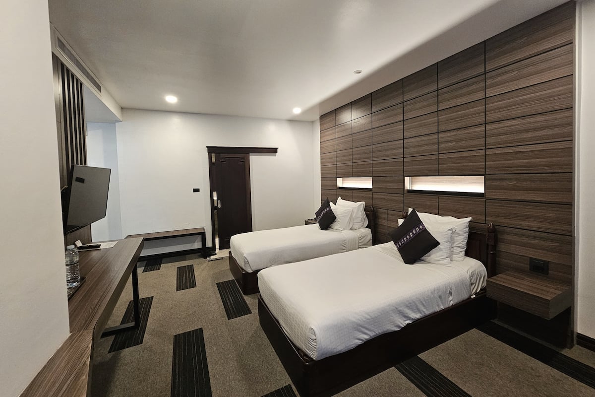 Une chambre d’hôtel avec deux lits, un bureau, une télévision et un mur décoratif en bois.