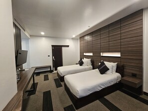 A hotel room with two beds, a desk, a TV, and a wooden accent wall. - Family Boutique Hotel (Vientiane)