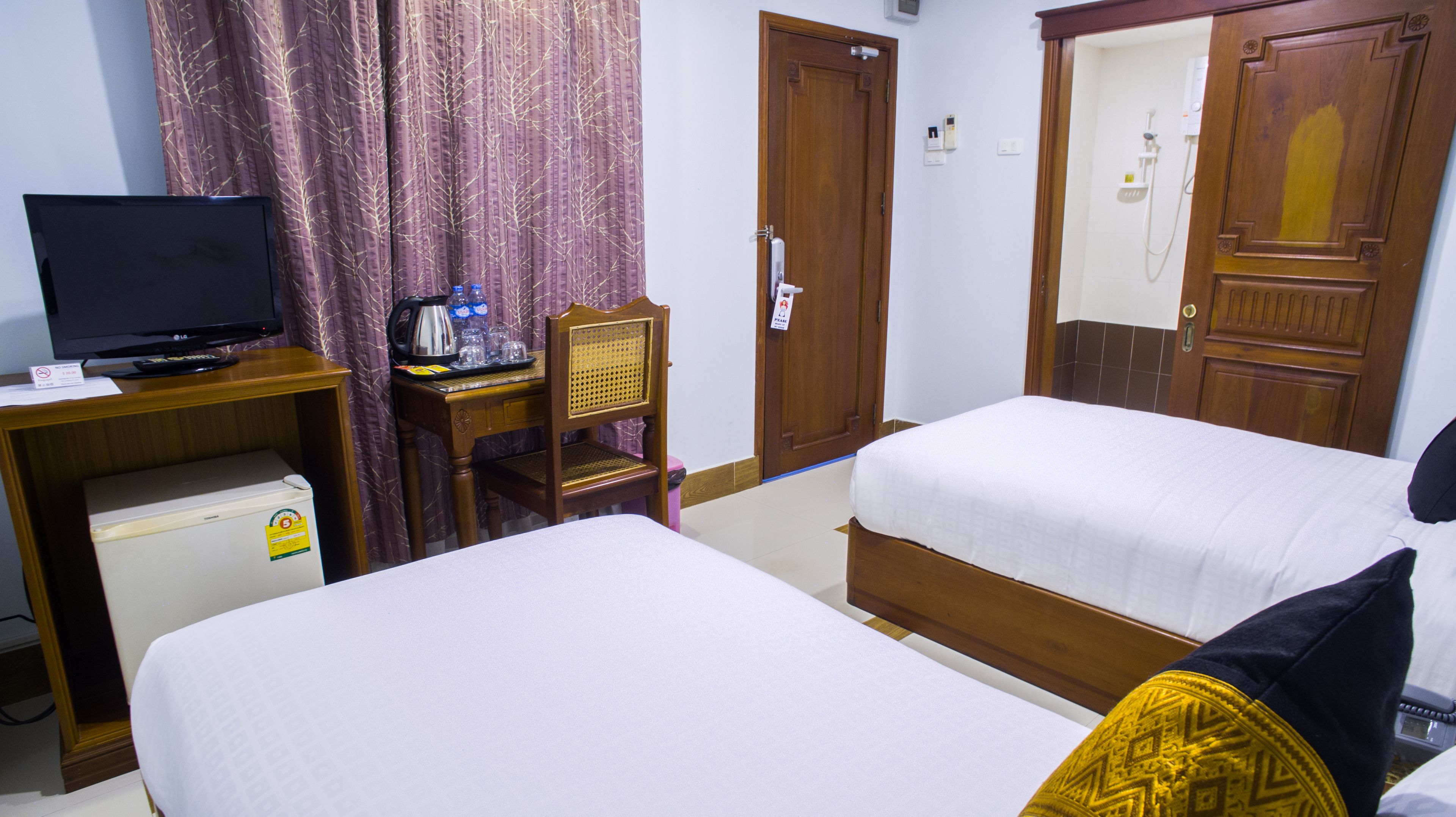 Une chambre d’hôtel avec deux lits simples, un bureau avec une télévision, une machine à café et un réfrigérateur.