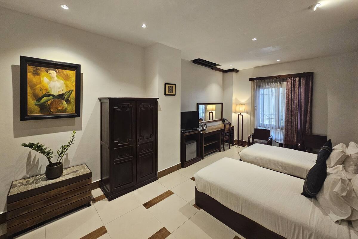 Une chambre d’hôtel avec un lit, un bureau, une télévision, une armoire et un tableau au mur.