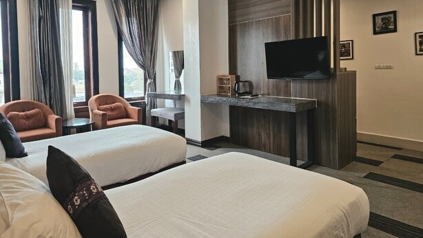 A hotel room with two beds, a flat-screen TV, a desk with a coffee maker, and a view of the outdoors through large windows. - Family Boutique Hotel (Vientiane)