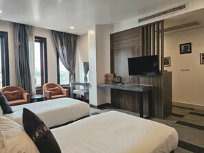 A hotel room with two beds, a flat-screen TV, a desk with a coffee maker, and a view of the outdoors through large windows. - Family Boutique Hotel (Vientiane)
