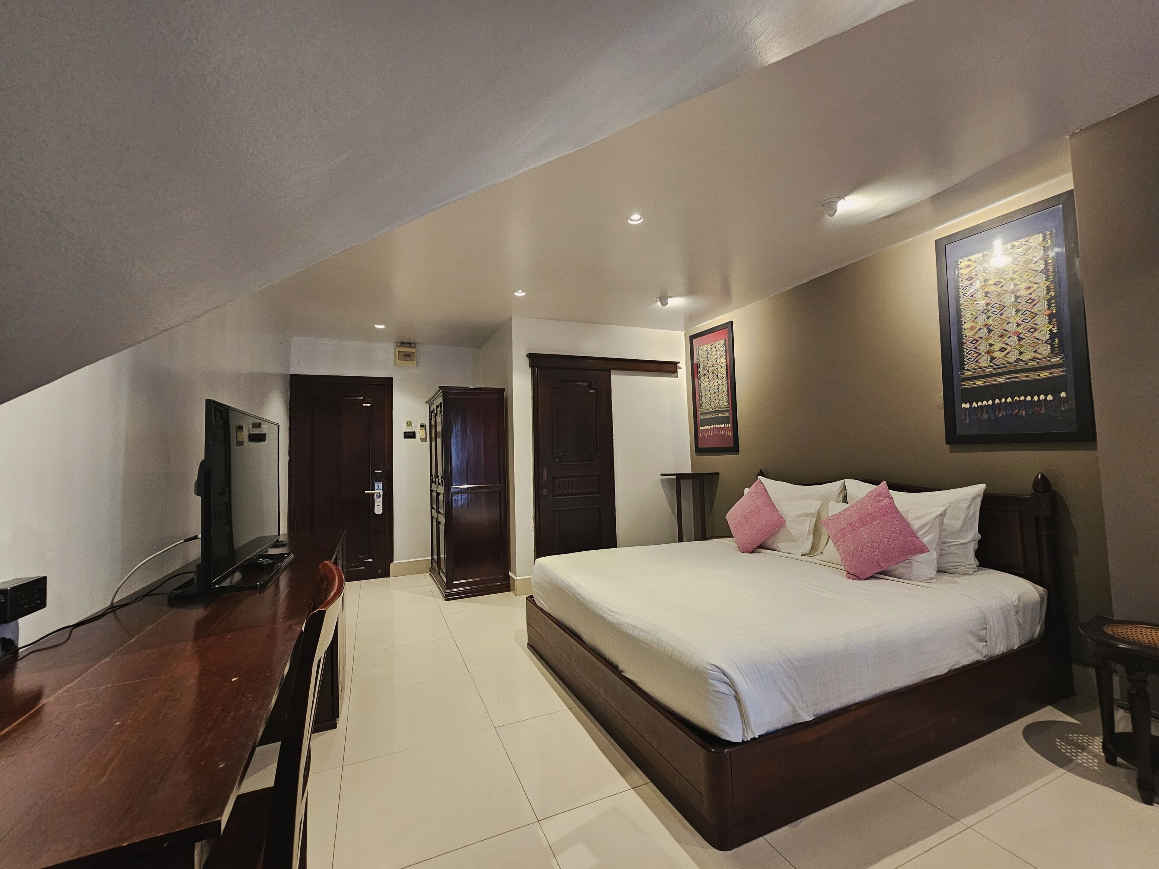 A hotel room with a bed, a desk, a TV, and a door.