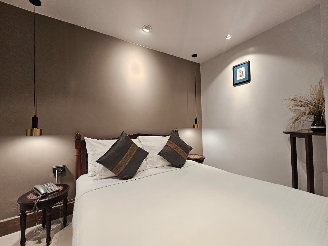 A bedroom with a large bed, bedside lamps, a bedside phone, and a small table with a plant.