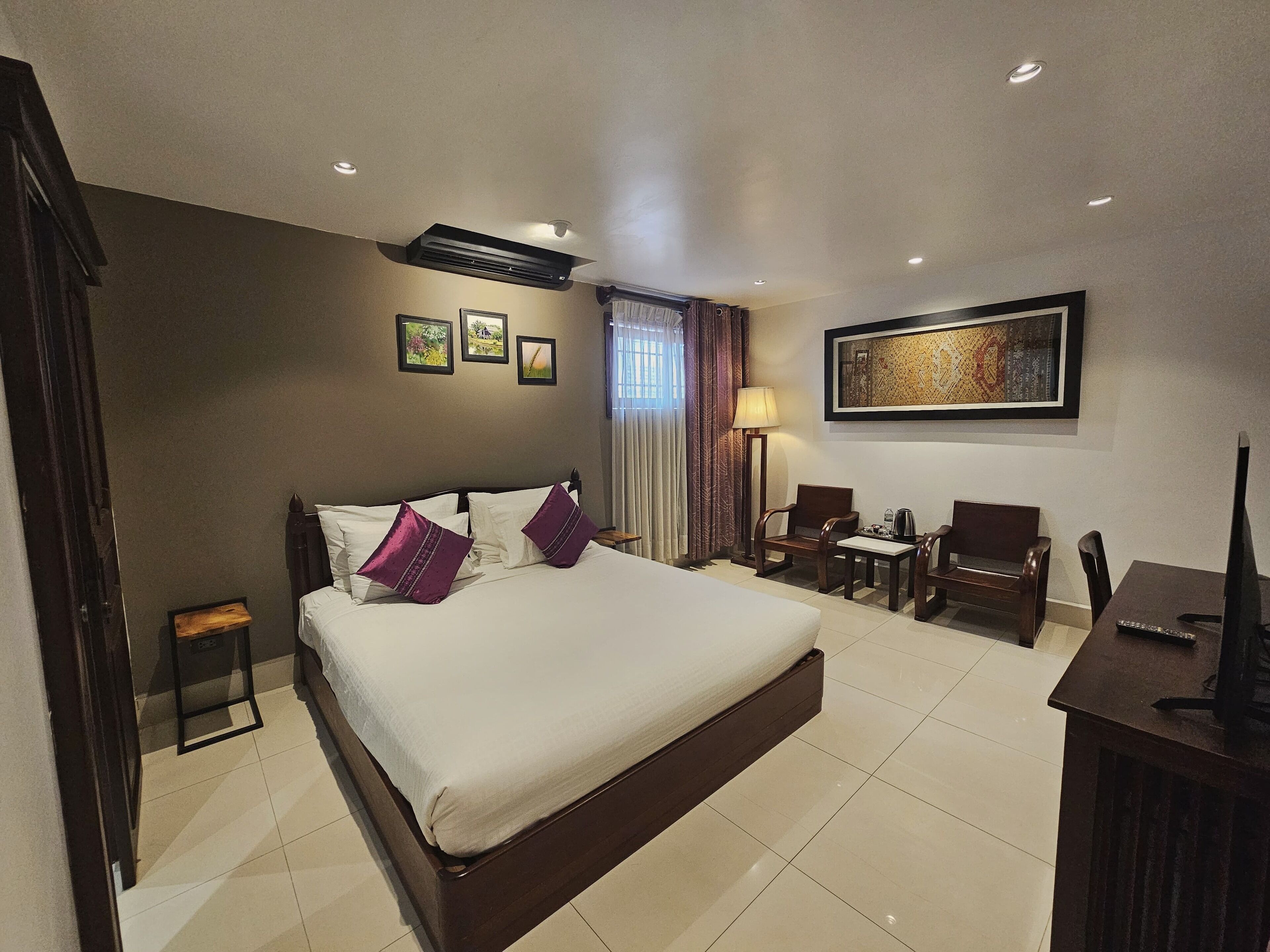 A hotel room with a large bed, two bedside tables, a desk with a chair, a TV, and a painting on the wall.