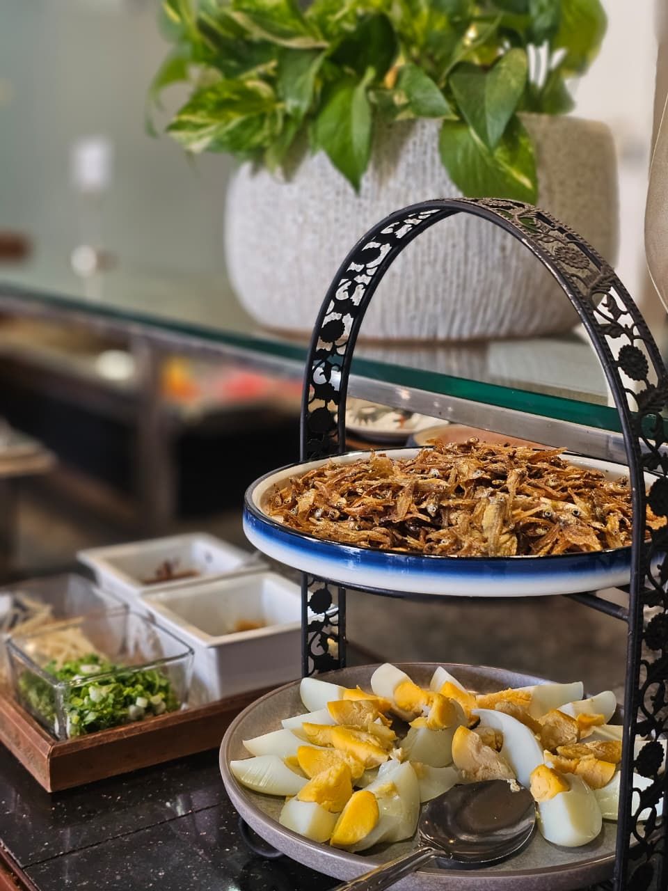 Una mesa de comedor con diversos alimentos, incluyendo un plato de pescado frito, una fuente de huevos cocidos en rodajas y un recipiente con verduras verdes.