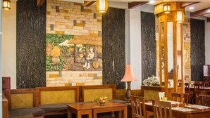 A restaurant with wooden furniture, a stone wall with a mural, and hanging lights. - Family Boutique Hotel (Vientiane)