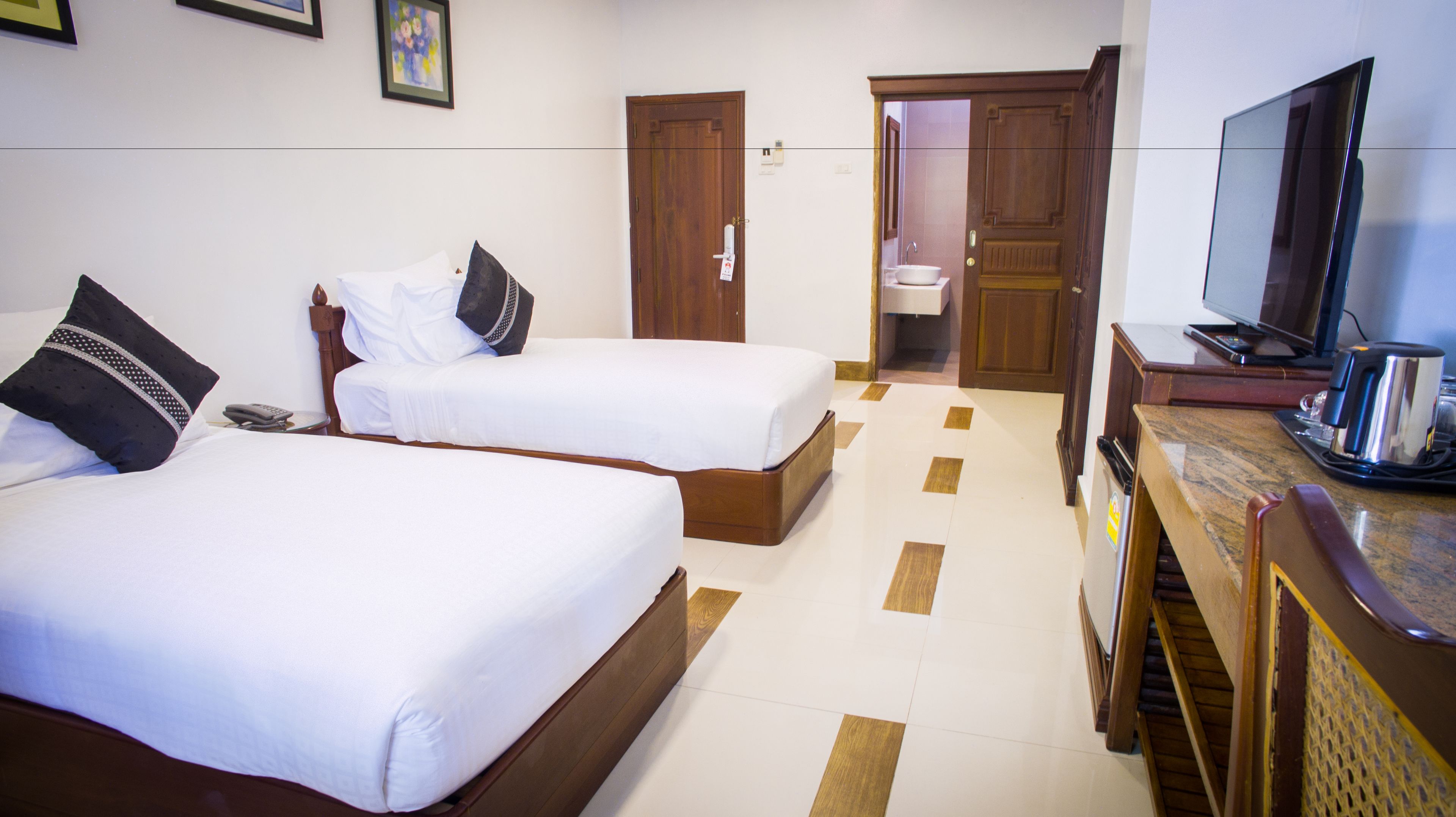 A hotel room with two beds, a television, a coffee maker, and a bathroom visible through an open door.