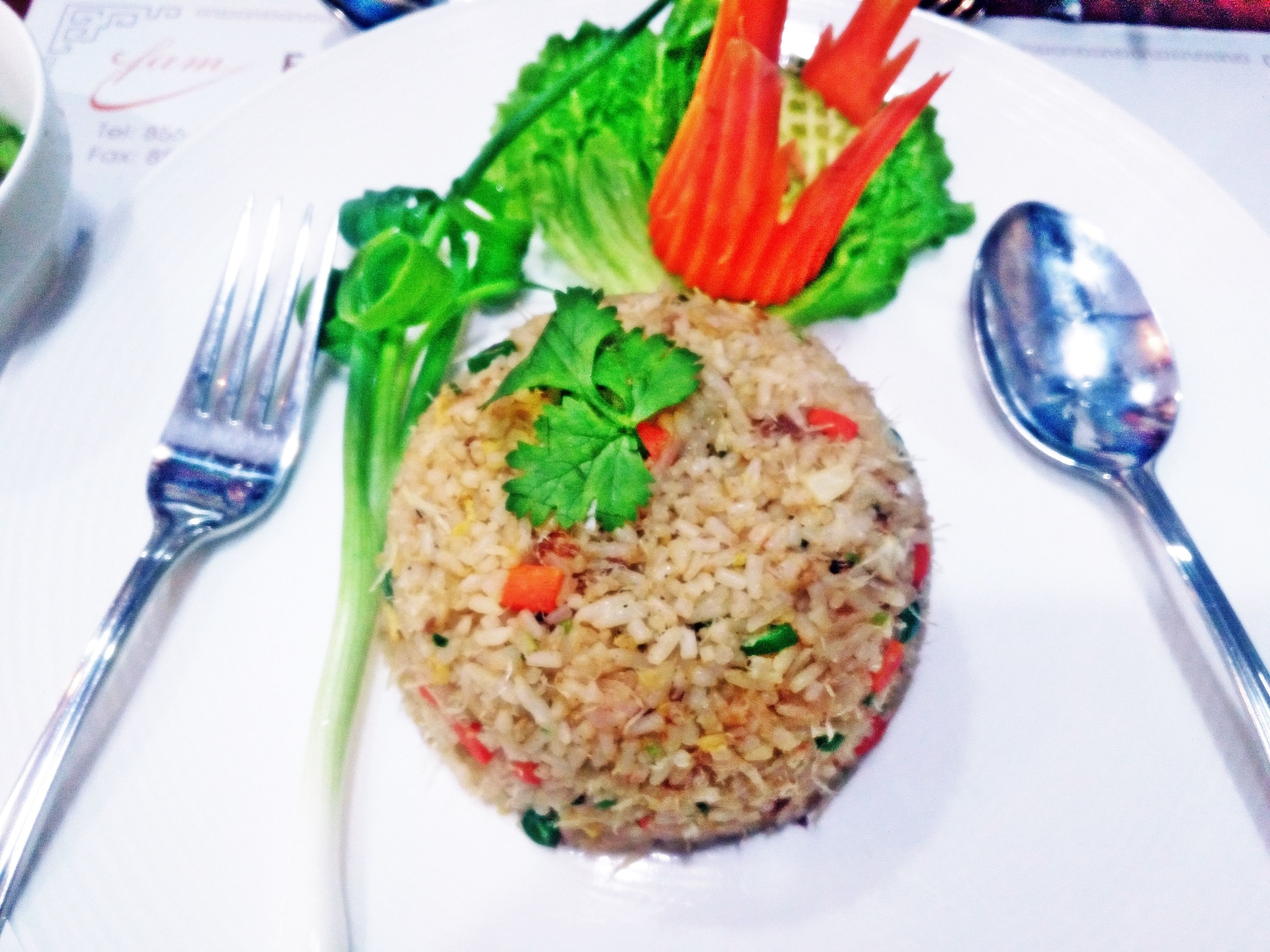Un plato de arroz frito con verduras y una hoja decorativa encima.