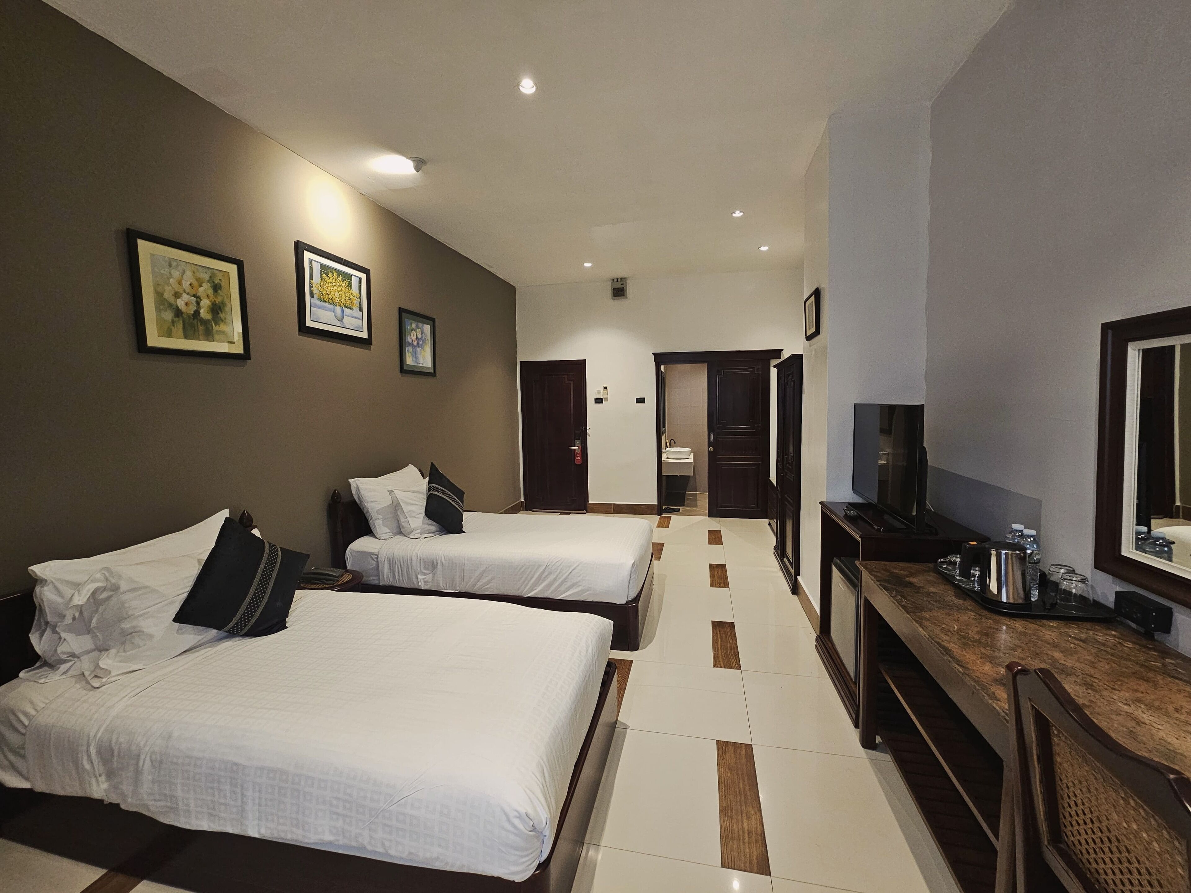 A hotel room with two beds, a TV, a desk with a mirror, and a bathroom visible through an open door.