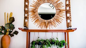 A wall-mounted mirror with a sunburst frame, flanked by two wooden sculptures, and a wooden console table below with hanging planters. - Family Boutique Hotel (Vientiane)