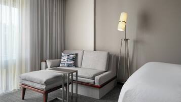 A modern hotel room with a sofa, a small table, a lamp, and a bed.