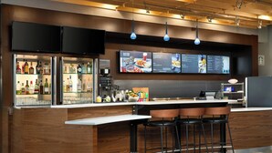 A modern bar area with a wooden bar counter, black stools, and a menu display above.