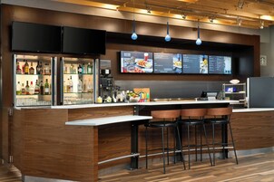 A modern bar area with a wooden bar counter, black stools, and a menu display above.