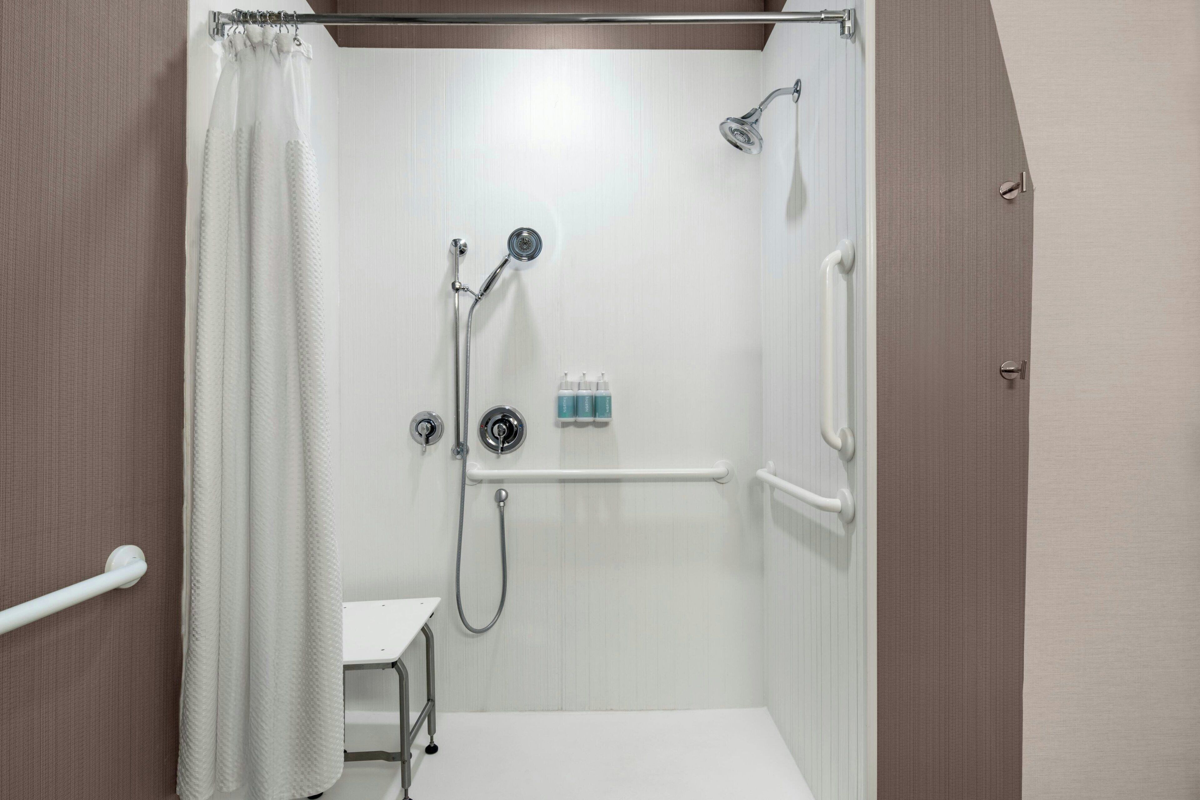 A small, enclosed shower area with a white showerhead, a handheld showerhead, and a handheld shower attachment. There is a white grab bar on the wall and a white towel rack.