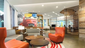 A modern lobby with orange seating, a central coffee table, and a mural of a vintage car. - Courtyard by Marriott Santa Monica (Santa Monica)