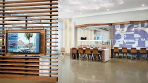 A modern hotel lobby with wooden slats, a reception desk, and a large digital screen displaying a cityscape. - Courtyard by Marriott Santa Monica (Santa Monica)